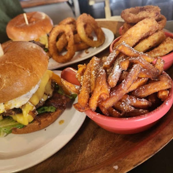 Two Gourmet Burger Bistro burgers with onion rings and sweet potato fries dusted with powdered sugar.