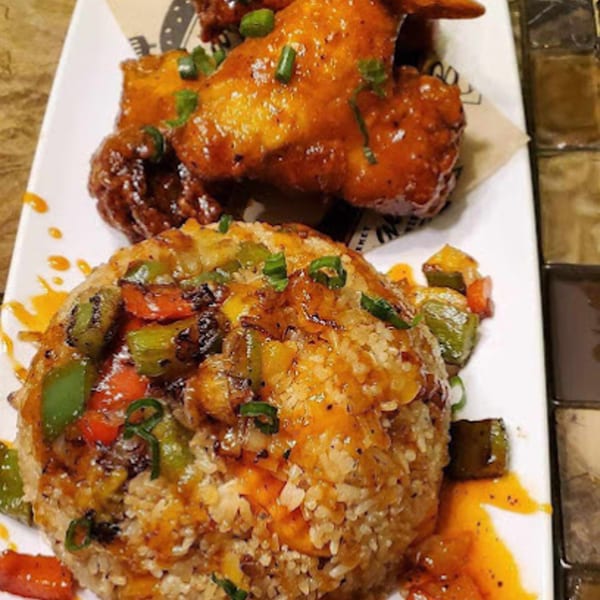 Sweet chili wings and a rice mound with bell peppers and scallions on a white plate.