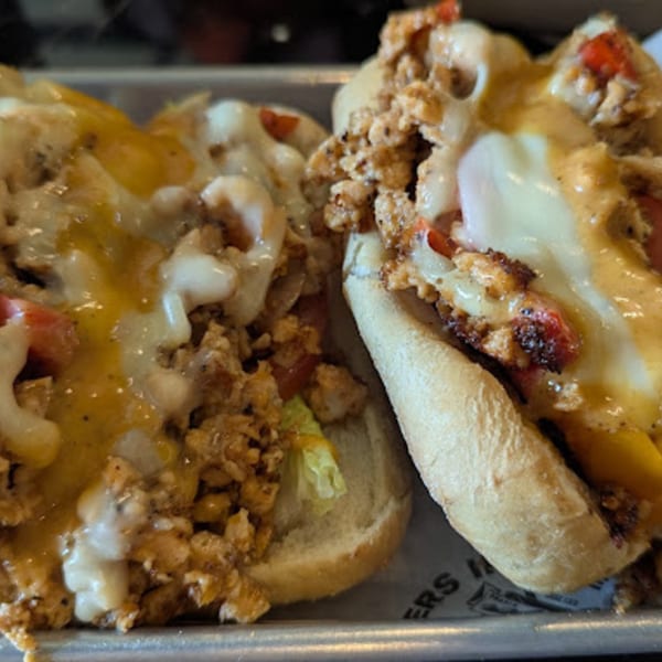 Two Gourmet Burger Bistro cheesesteak sandwiches, overflowing with meat, melted cheese, and red peppers.